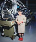 Woman standing next to a large industrial embroidery machine in a factory setting