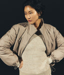 Woman wearing a beige jacket over a textured sweater against a black background