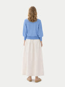 back view of a woman wearing a blue sweater and white skirt on a white background #color_azure-blue