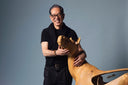 Naoki Takizawa smiling, his hands resting on a carved wooden horse, in a photo studio