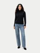 front view of a woman wearing a black turtleneck and blue jeans on a white background #color_black