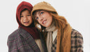Two people wearing winter clothing and hats against a white background