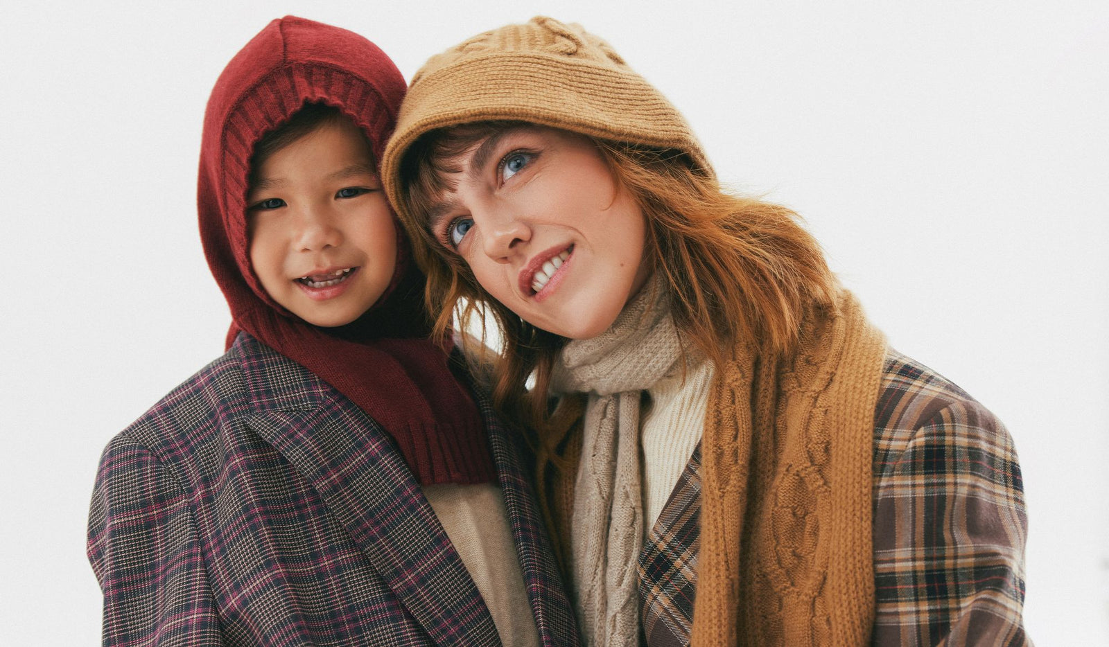 Two people wearing winter clothing and hats against a white background