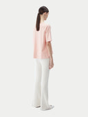 back view of a woman wearing a pink cashmere t-shirt and white pants #color_primrose-pink