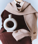 Knitted brown and beige scarf with a white vase on a light blue background