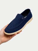 Navy blue loafer shoe held in a hand against a light gray background #color_navy