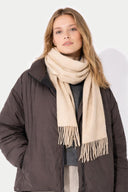 Woman wearing a beige scarf and dark coat against a white background