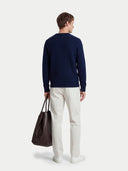 Man wearing a navy sweater and white pants, holding a black bag on a white background #color_navy