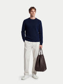 Man wearing a navy sweater and white pants, holding a brown leather bag on a white background #color_navy