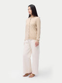 side view of a woman wearing a beige cardigan and white pants on a white background #color_beige