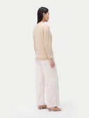 back view of a woman wearing a beige sweater and white pants on a white background #color_beige