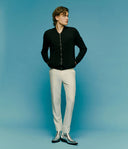 Man wearing a black jacket and white pants against a blue background