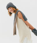 Woman wearing a beige sleeveless sweater, gray knit hat, and gloves on a white background