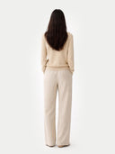 back view of a woman wearing a beige sweater and cream pants on a white background.