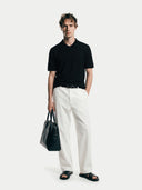 front view of a man wearing a black polo shirt and white pants holding a black bag on a white background #color_black