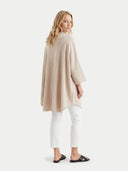 back view of a woman wearing a beige poncho over a white outfit on a white background #color_all