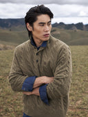Man in an olive cable-knit cashmere polo jumper over a denim shirt on the steppe