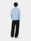 Person wearing a light blue cashmere sweater, black pants, and white shoes on a white background