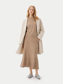 Woman wearing a beige coat, sweater, and a long skirt on a white background #color_warm-grey