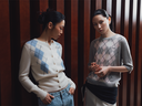 Two women wearing argyle pattern sweaters in front of a striped wall.
