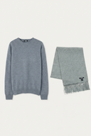 A light gray knit crewneck sweater displayed next to a matching fringed scarf with a small black embroidered logo, set against a solid off-white background.