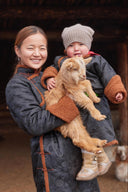 A Mongolian mother holding her baby and a young cashmere goat
