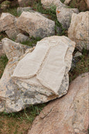 A cream knitted cashmere vest with a traceability tag laid on a lichen-covered rock