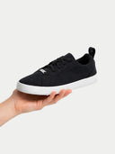 Black sneaker with white sole held in a hand against a light gray background #color_black
