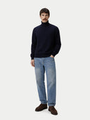 front view of a man wearing a navy turtleneck sweater and light blue jeans on a white background #color_navy-blazer
