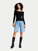 Woman wearing a black long-sleeve top, light blue denim shorts, and black knee-high boots on a white background #color_black