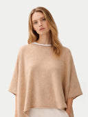 Woman wearing a beige poncho over a white top on a light gray background #color_beige