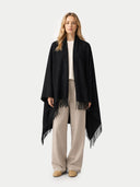 Woman wrapped a black blanket with fringe on a white background.