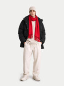Person wearing a black coat, red scarf, white beanie, and beige pants on a white background