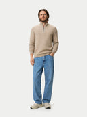 Man wearing a beige half-zipper sweater and blue jeans on a white background #color_warm-grey