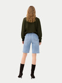 back view of a person wearing a green sweater and light blue denim shorts on a white background #color_capulet-olive
