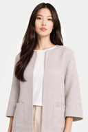 Woman wearing a light gray crew neck poncho jacket with side pockets over a white shirt on a plain background #color_dawn-blue
