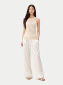 Woman wearing a beige sleeveless top and white pants on a white background #color_off-white