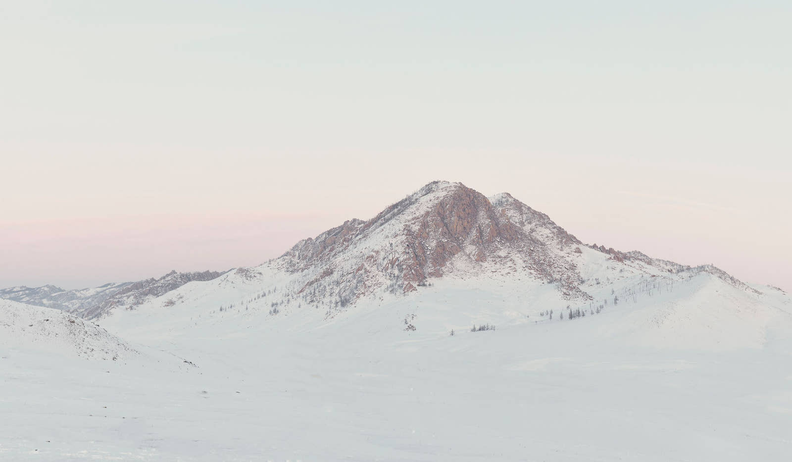 Snow-covered mountain peak under a light pink sky. desktop