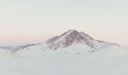 Snow-covered mountain peak under a light pink sky. desktop