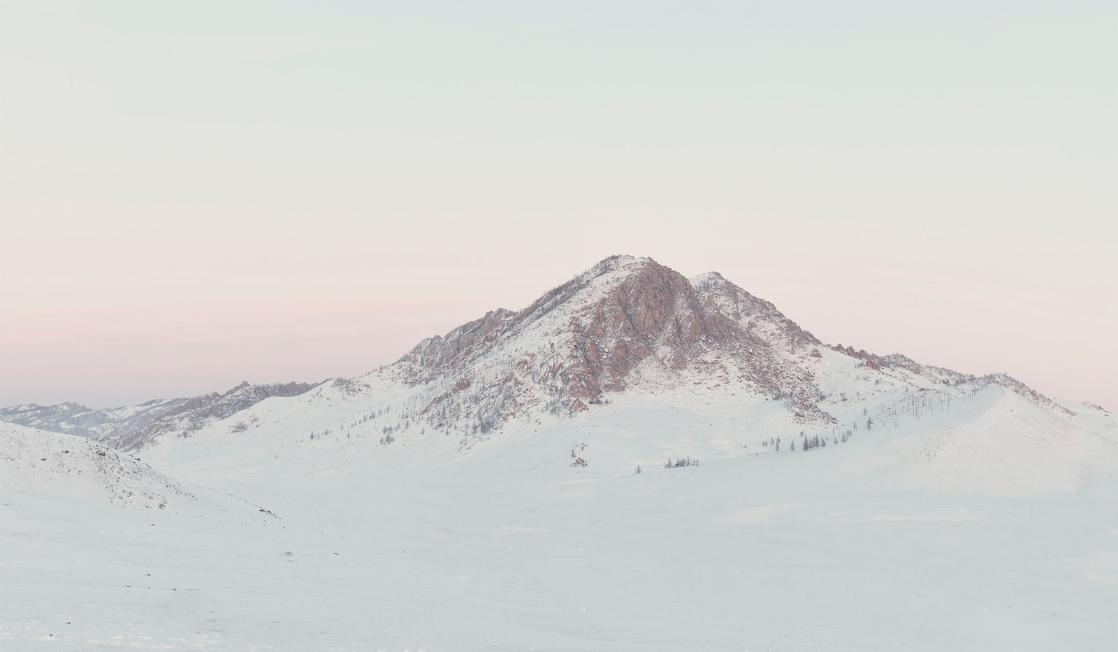Snow-covered mountain peak under a light pink sky. desktop