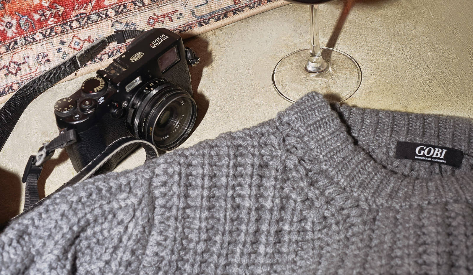 Gray sweater with 'GOBI' label next to a camera and wine glass on a textured surface. desktop