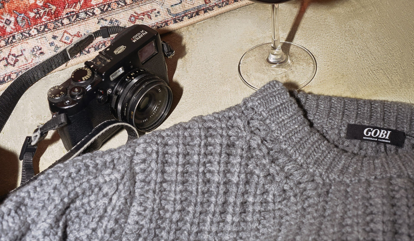 Gray sweater with 'GOBI' label next to a camera and wine glass on a textured surface. desktop