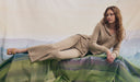 Woman in beige outfit sitting on a green surface with a scenic background. desktop