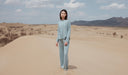 Woman in a light blue outfit standing in a desert landscape with mountains in the background. desktop