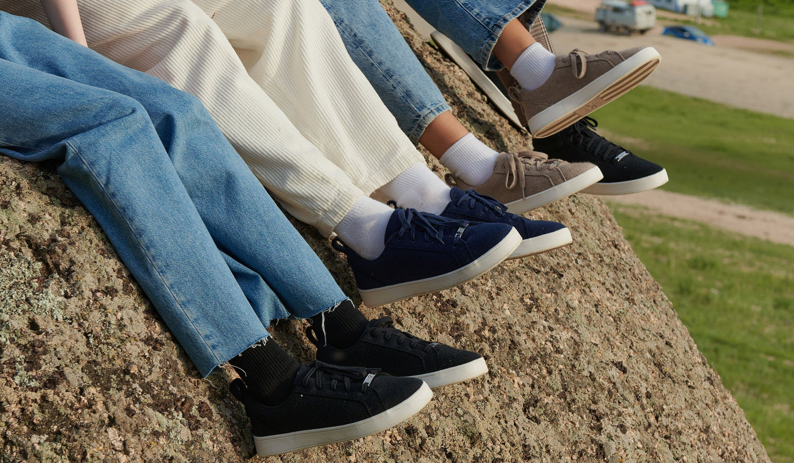 People sitting on a rock wearing jeans and sneakers with a grassy area in the background. desktop