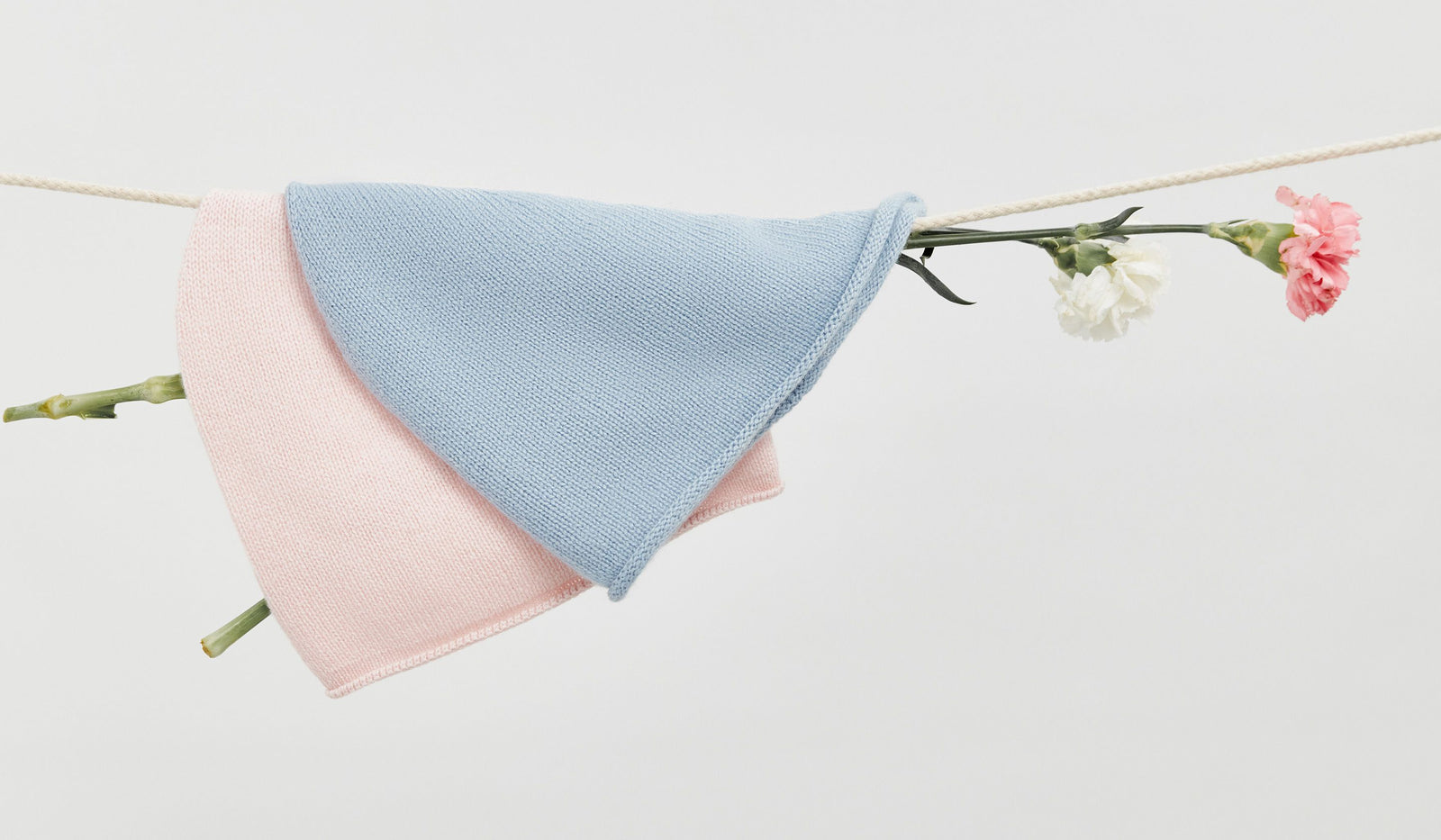 Baby blanket with pink and blue layers draped over a branch with flowers on a light gray background. desktop