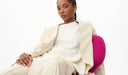 Woman in a beige suit sitting on a pink chair against a white background. desktop