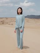Person wearing a light blue outfit standing in a desert landscape with mountains in the background. mobile