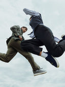 Two people in casual clothing jumping against a cloudy sky.  mobile