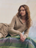 Woman wearing a beige sweater sitting on a bed with a blurred background. mobile